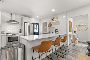 Een moderne keuken met witte kasten, roestvrijstalen apparatuur en een centraal eiland met barkrukken.