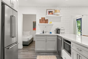 A modern kitchen with white cabinetry, a stainless steel refrigerator, and a built-in oven. There is a small island with a sink and a decorative shelf above it.