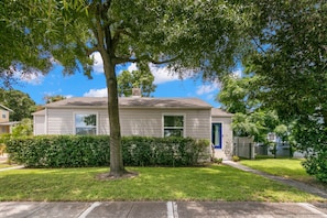 A single-story house with a front yard, a tree, and a blue door.