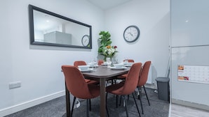 A modern dining area with a round table, six chairs, a vase of flowers, two wall clocks, and a calendar on the wall. - Sunrise Haven Sleeps 7 With Parking (Gravesend)