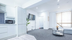 A modern living room with a grey carpet, white cabinetry, a flat-screen TV, a round coffee table, and a grey sofa. - Sunrise Haven Sleeps 7 With Parking (Gravesend)