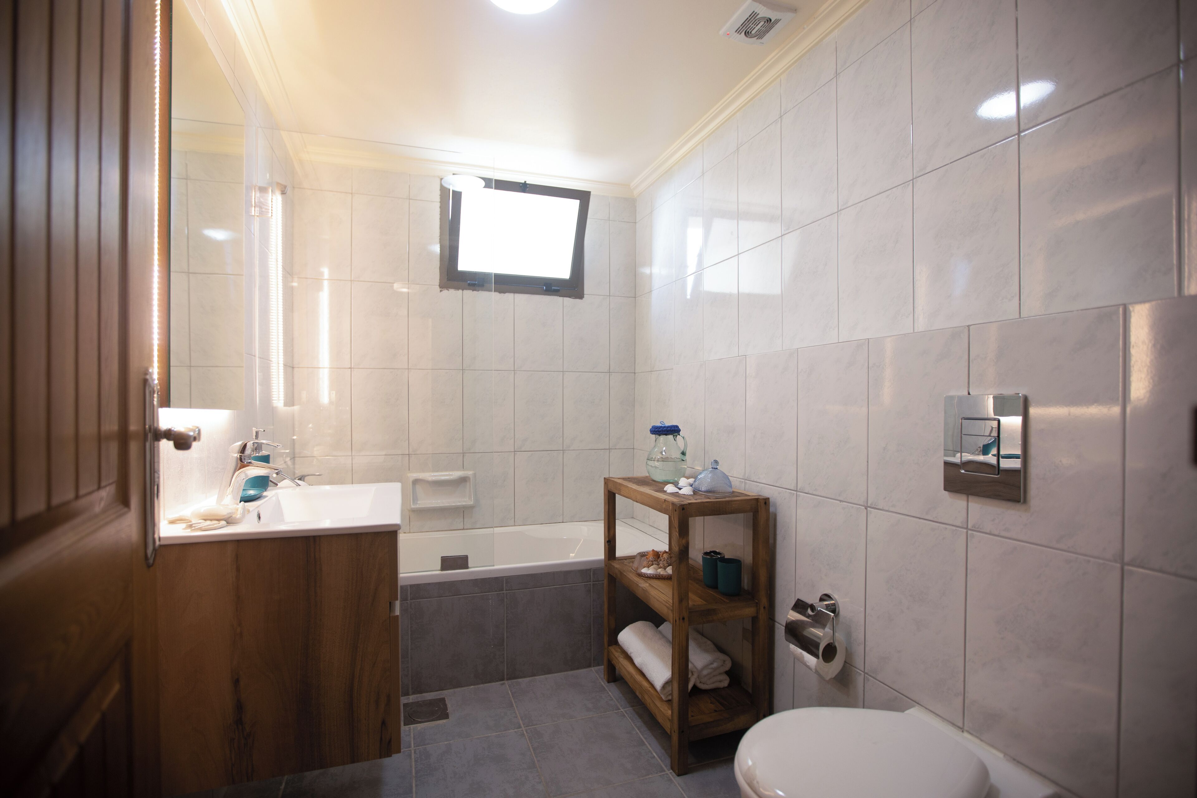 Un baño con tocador de madera, bañera, inodoro y estante con artículos de tocador.
