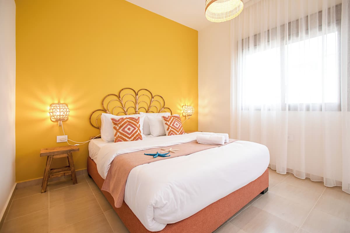 A hotel room with a bed, a nightstand, and a window with sheer curtains.