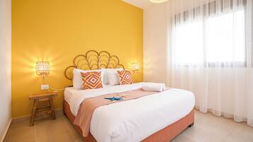 A hotel room with a bed, a nightstand, and a window with sheer curtains.