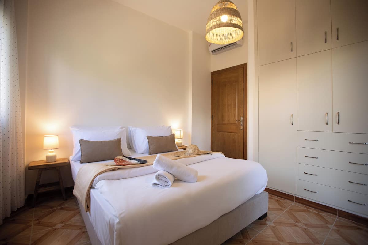 A neatly made bed with pillows, a bedside lamp, a wooden nightstand, and a wardrobe with multiple drawers.