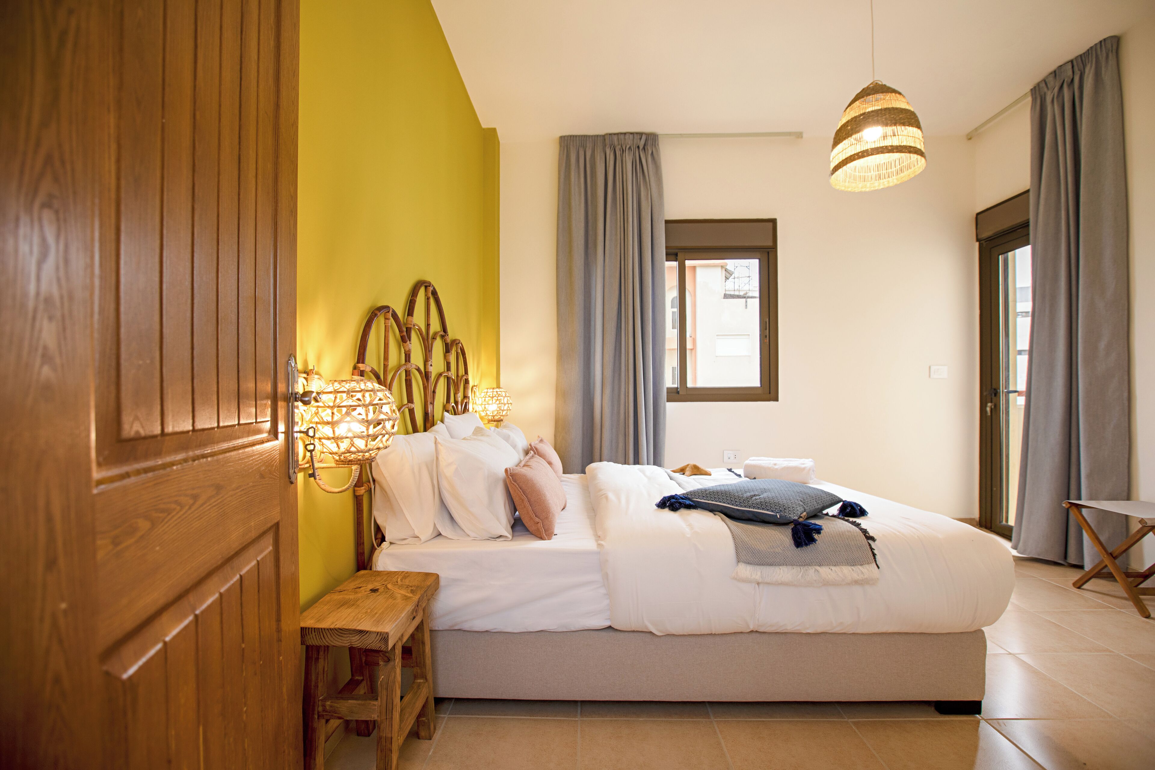 A bedroom with a bed, bedside lamps, a wooden bench, and a window with curtains.