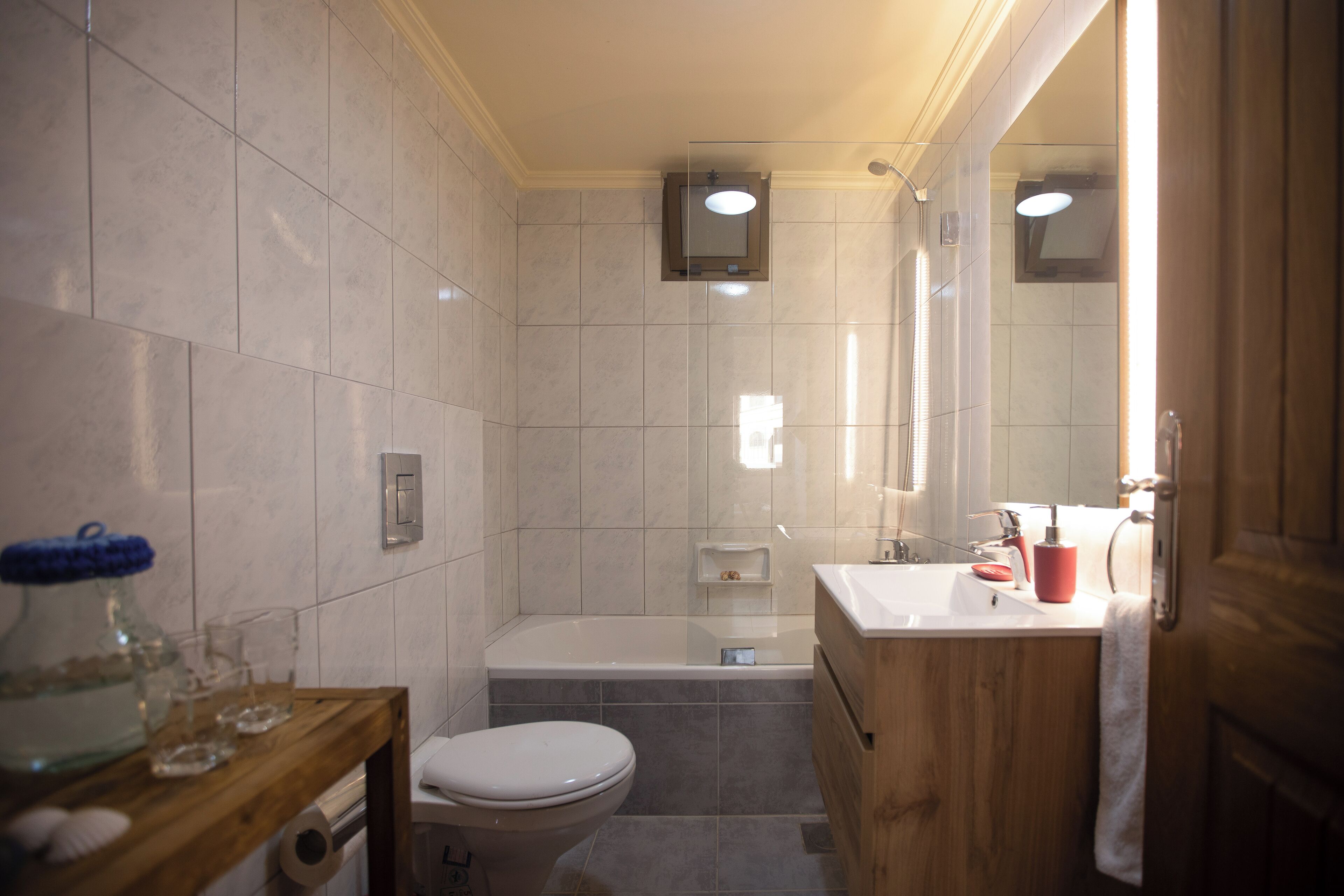 A bathroom with a toilet, bathtub, and sink. There is a mirror above the sink and a showerhead above the bathtub.