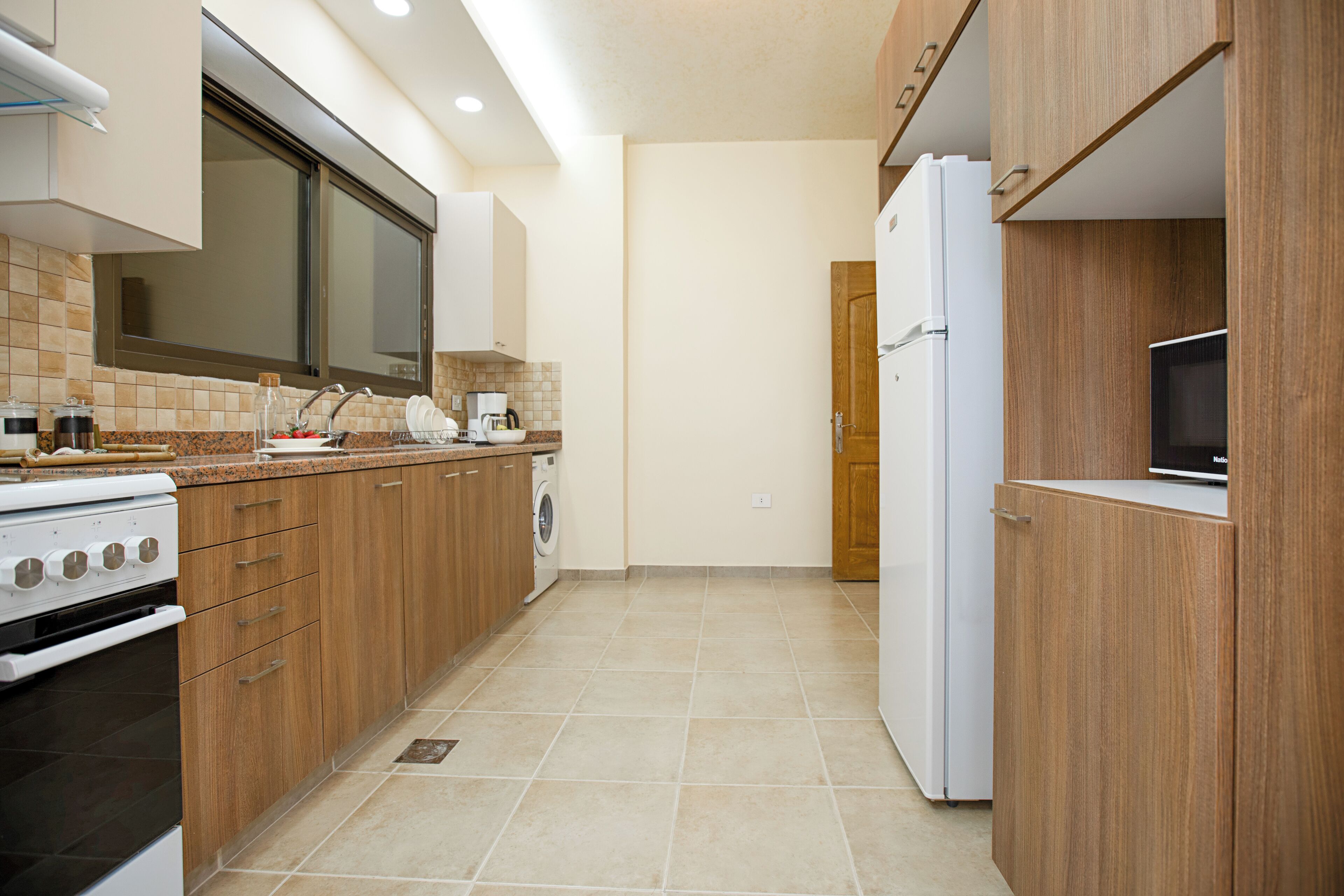 A modern kitchen with wooden cabinets, a built-in oven, a washing machine, and a refrigerator.