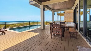 Une terrasse en bois avec une piscine, un espace salon extérieur et une vue sur l’océan.