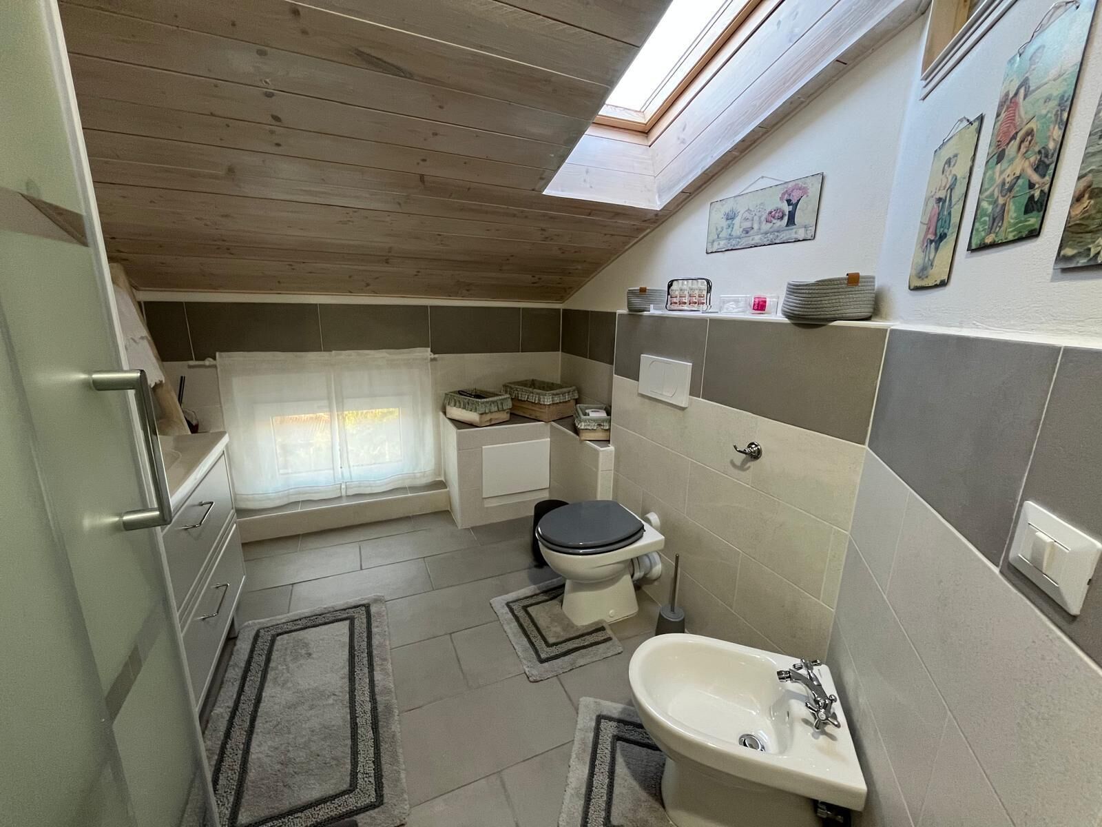 Een kleine badkamer met dakraam, toilet, wastafel en bad.