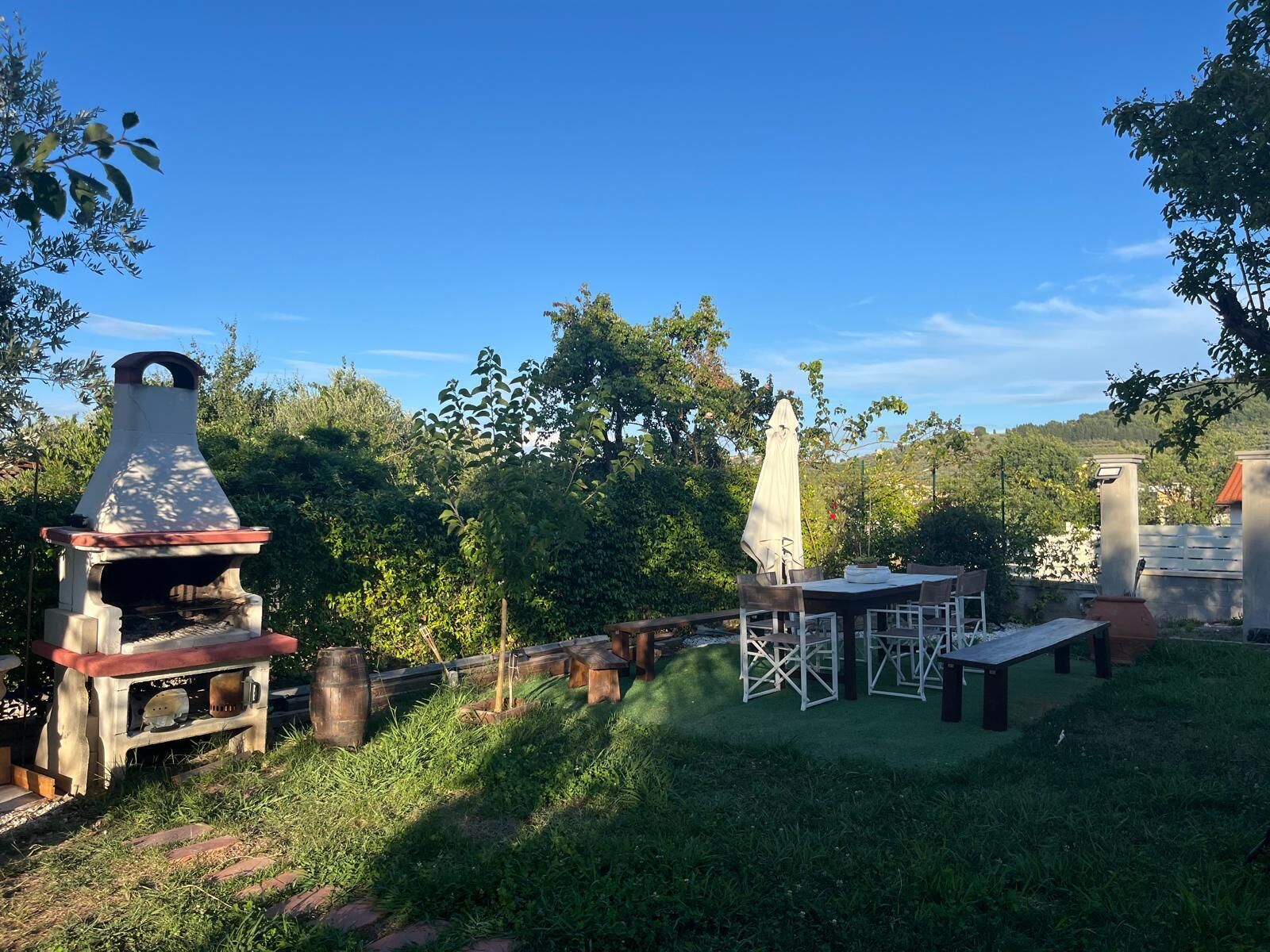 Patio esterno con barbecue, tavoli e sedie di legno.