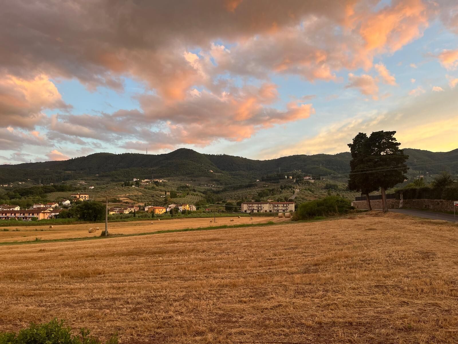 A rural landscape with a field, a few buildings, and hills in the background.