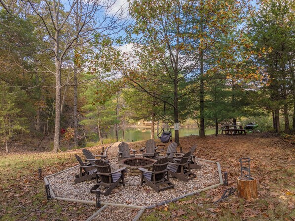 A circular seating area with Adirondack chairs around a central fire pit, surrounded by a gravel circle.