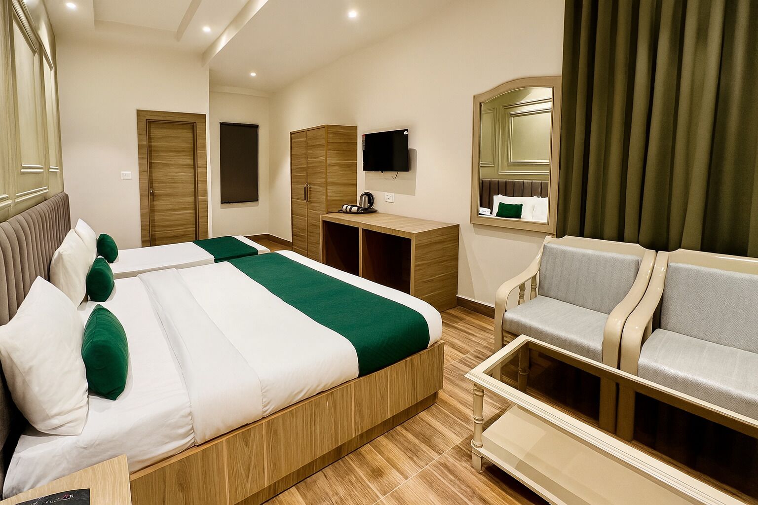 A hotel room with two beds, a desk, a TV, and a seating area.
