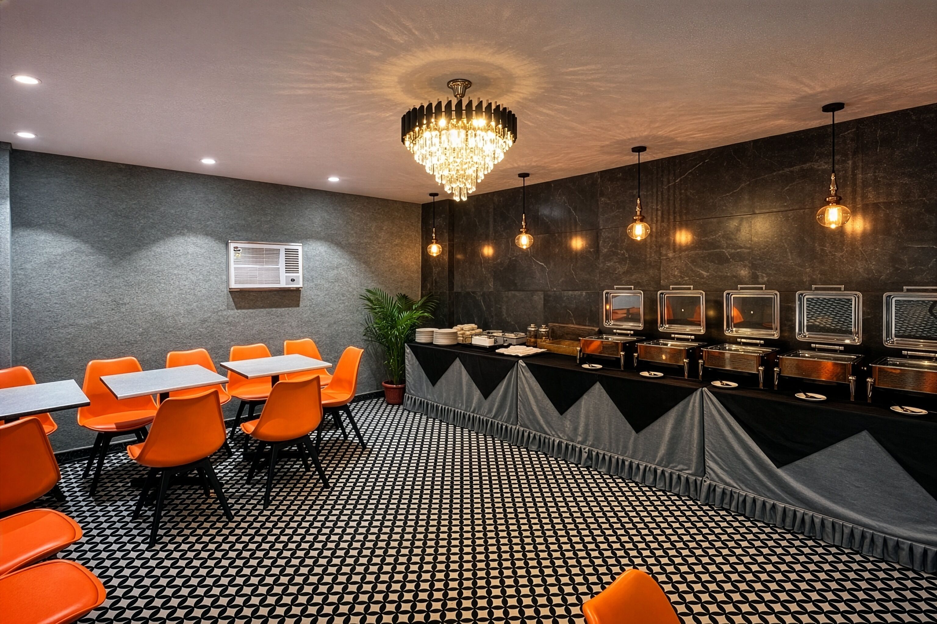 Un salón de conferencias con suelo a cuadrícula blanco y negro, sillas anaranjadas, una mesa larga con mantel negro, una araña y unidades de aire acondicionado fijadas a la pared.