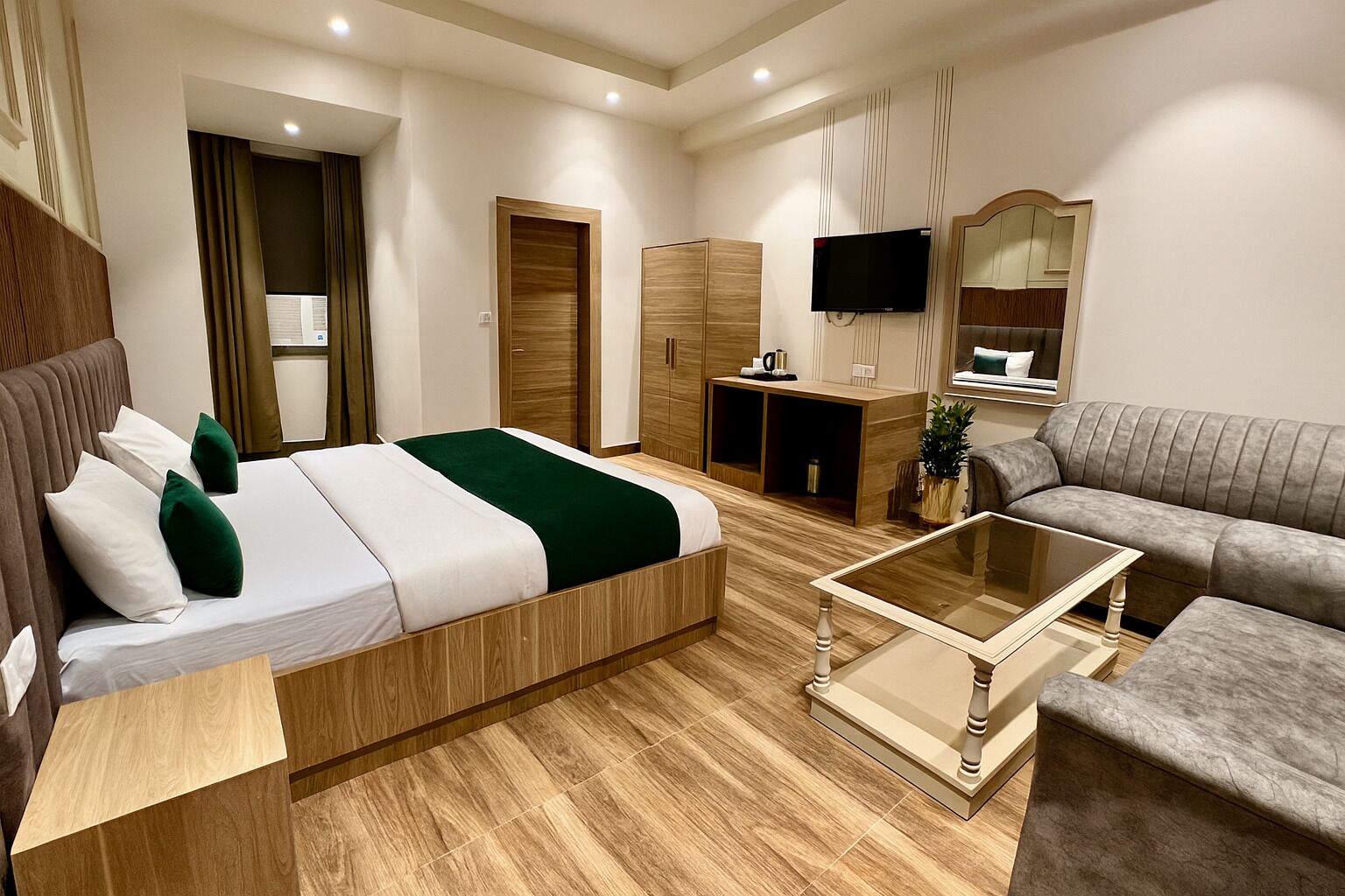 A modern hotel room with a bed, a sofa, a TV, a desk, and a mirror.