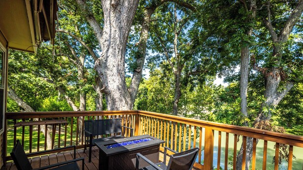 Una terraza de madera con una mesa y sillas, con vista a un lago rodeado de árboles.