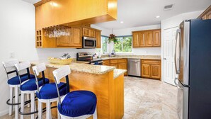 Una cocina moderna con armarios de madera, un refrigerador de acero inoxidable y una isla central con taburetes de bar.