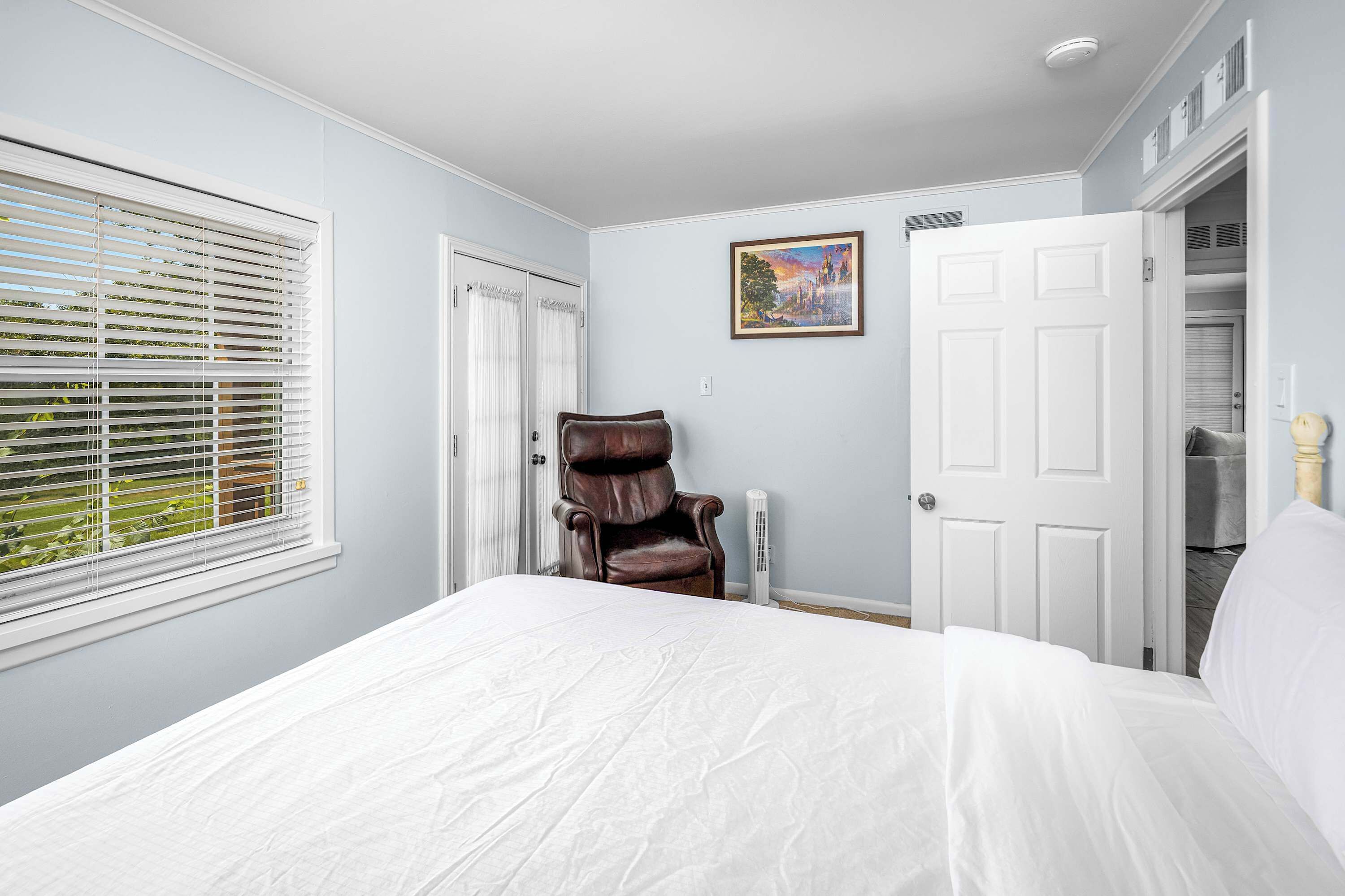 Een slaapkamer met een groot bed, een fauteuil, een witte deur en een schilderij aan de muur.