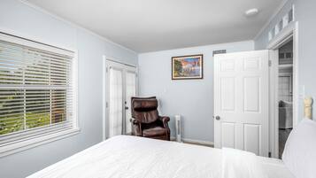 Een slaapkamer met een groot bed, een fauteuil, een witte deur en een schilderij aan de muur.