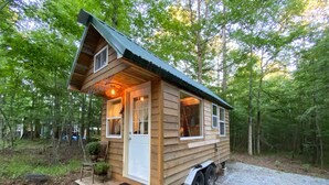 Una pequeña cabaña de madera con un porche, una puerta corredera y una ventana.
