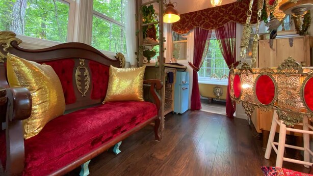 Una habitación con un sofá de terciopelo rojo, un aparador de madera y un espejo decorativo.