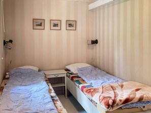 Una stanza con due letti singoli, un comodino, una lampada e tre quadri appesi al muro.