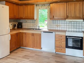 A kitchen with wooden cabinets, a dishwasher, a stove, and a window with a view of greenery.