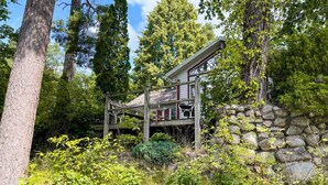 Un chalet rustique doté d’une terrasse en bois, d’un mur en pierre et d’une végétation luxuriante.