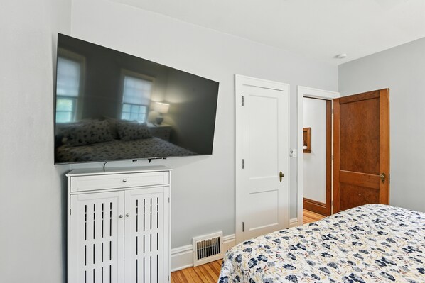 A bedroom with a bed, a TV mounted on the wall, a wardrobe, and a door.