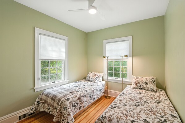 A bedroom with two beds, a ceiling fan, and windows with blinds.