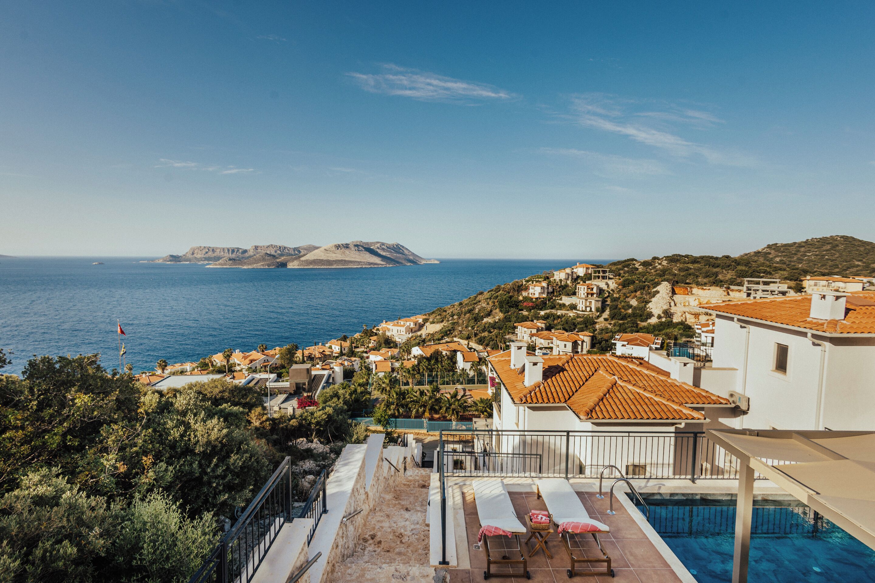 A rooftop pool area with a view of the sea and a hillside town.