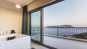A modern bathroom with a bathtub, a glass shower enclosure, and a balcony with a view of the sea and mountains.