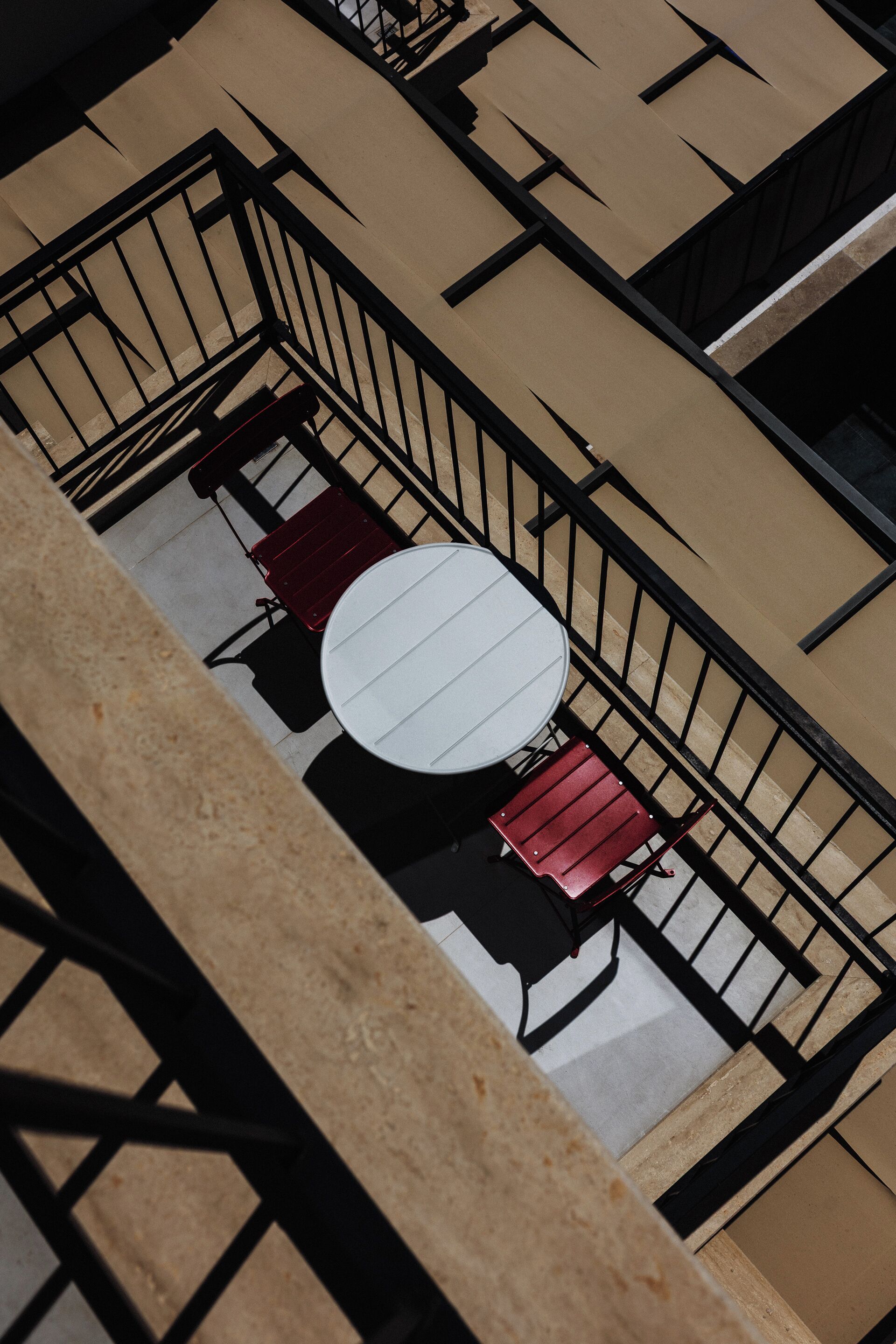 Eine Vogelperspektive zeigt eine Dachterrasse mit einem runden Tisch und zwei roten Stühlen, umgeben von schwarzen Geländern.