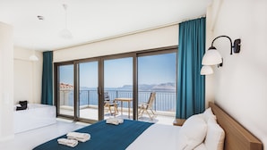 A hotel room with a large bed, a bathroom, a balcony with a table and chairs, and a view of the sea.