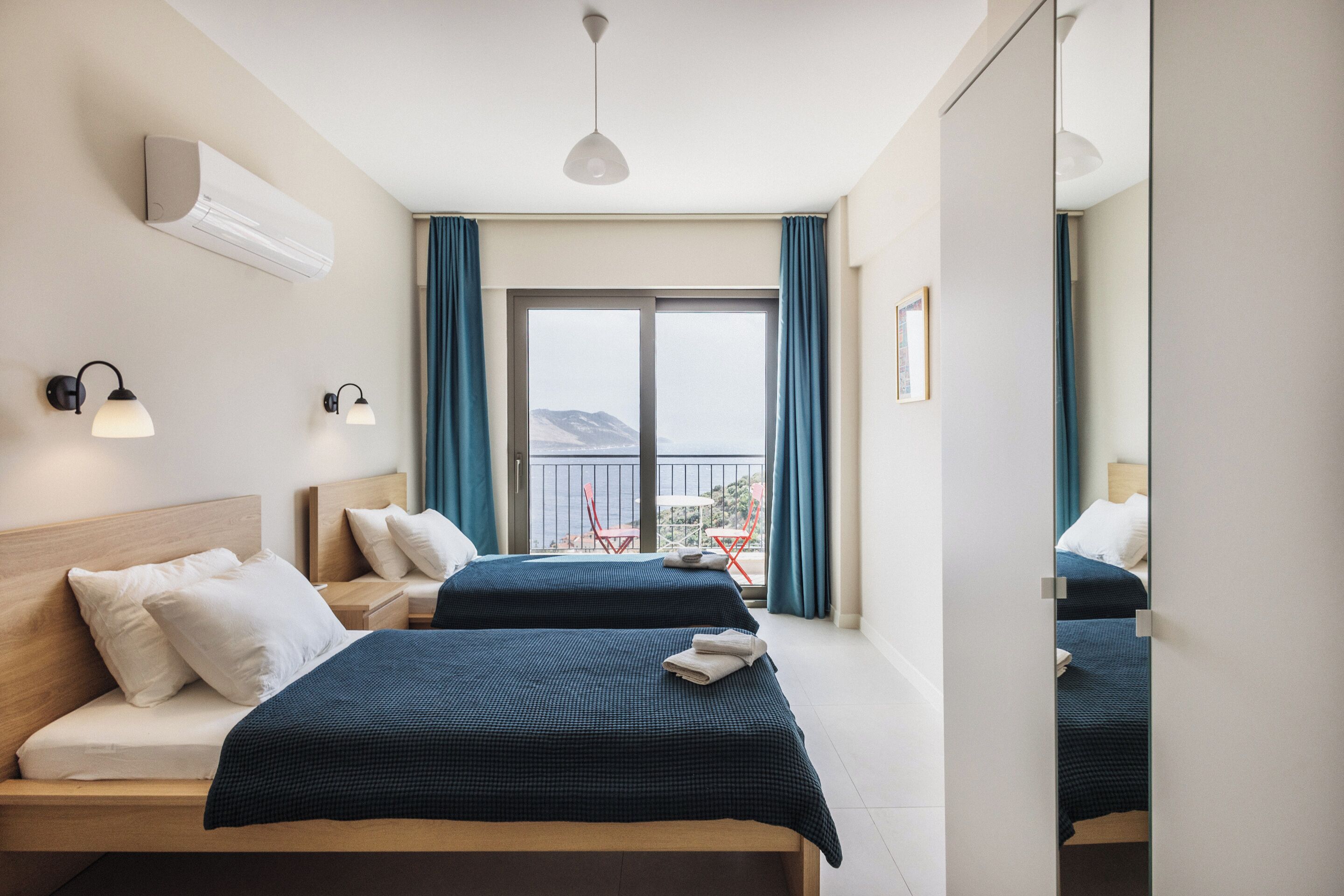 A hotel room with two beds, a balcony with a view, and a large mirror.