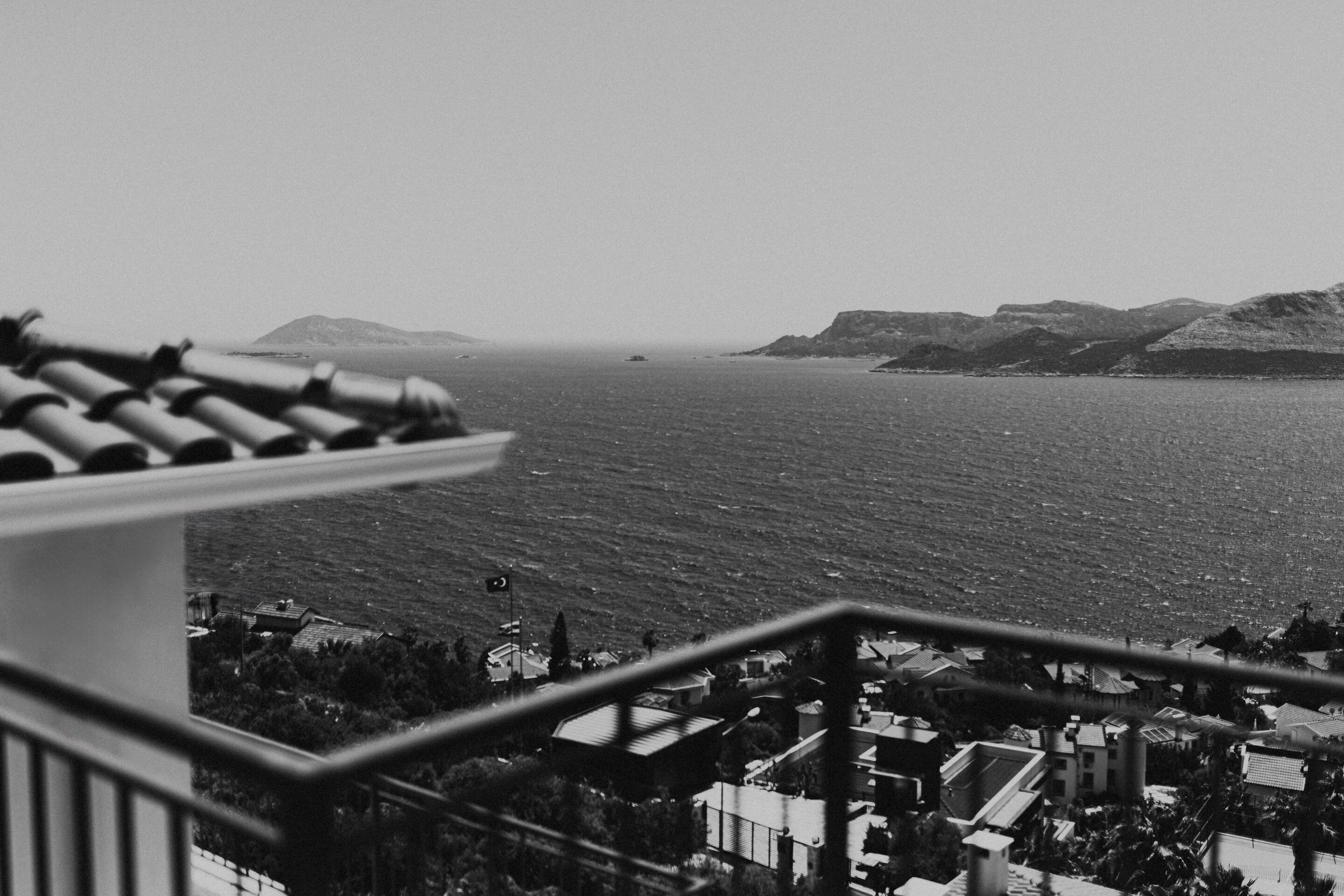 A coastal view with a railing in the foreground, a body of water, and distant landforms.