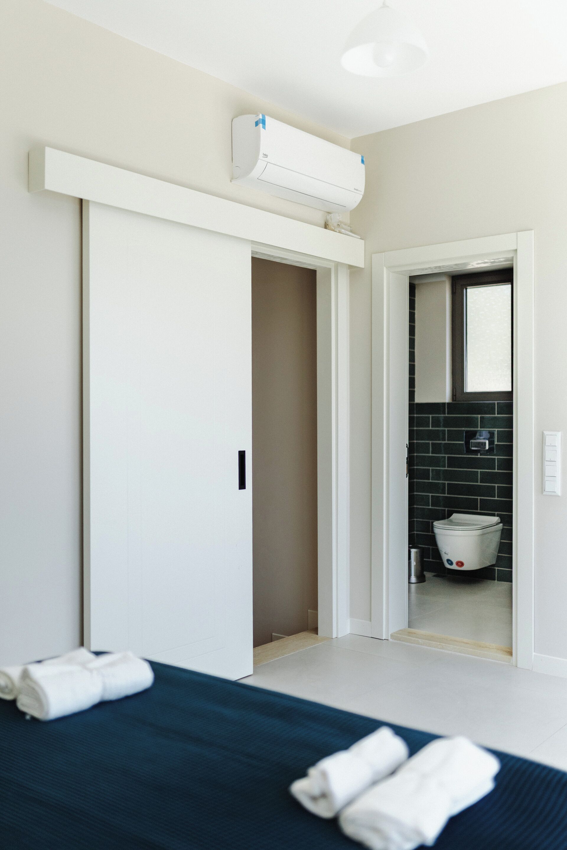 Ein Hotelzimmer mit Bett, einem weißen Kleiderschrank, einem Badezimmer mit Toilette und Spiegel sowie einer Klimaanlage an der Wand.