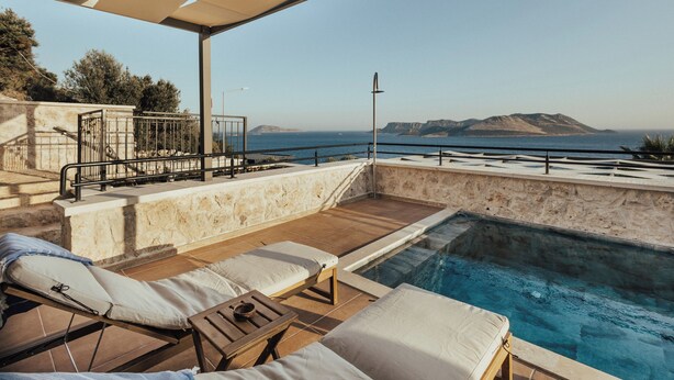A pool area with lounge chairs and a view of the sea.