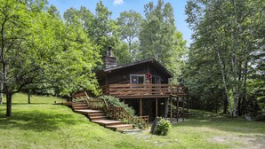 Une cabane en bois dotée d’un porche et d’un escalier menant à l’entrée, entourée d’arbres.