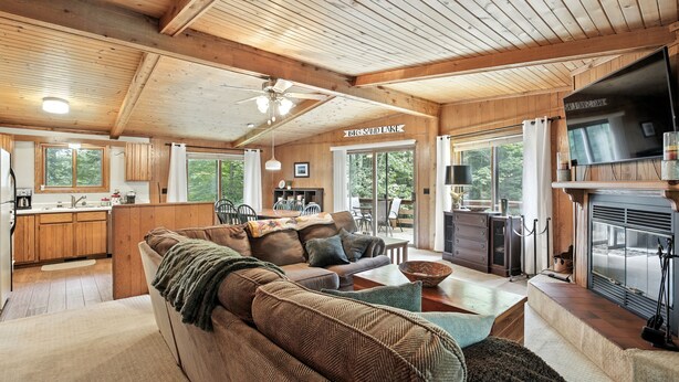 L’intérieur chaleureux d’un chalet avec un grand plafond en bois, un coin repas, une cheminée et un panneau indiquant qu’on peut admirer la vue sur le lac Big Sand.