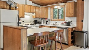 Une cuisine avec des armoires en bois, un réfrigérateur en acier inoxydable, un four à micro-ondes, une cuisinière et un évier. Il y a deux chaises en bois près de l’îlot central.