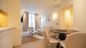 A modern living room with a sofa, chairs, a dining table, and a TV. - Elegant Apt With AC - 2br-6p -palais Garnier (Paris)