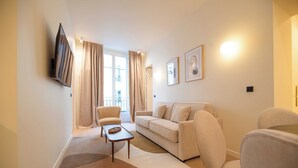 A modern living room with a sofa, chairs, a coffee table, and a flat-screen TV mounted on the wall. - Elegant Apt With AC - 2br-6p -palais Garnier (Paris)
