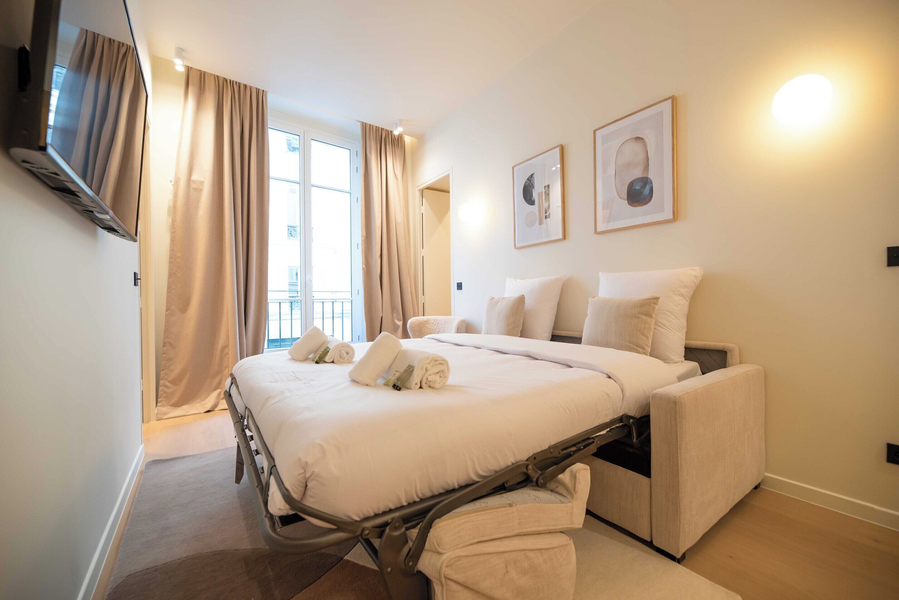 Ein Hotelzimmer mit einem Bett, einem an der Wand befestigten Fernseher und einem Fenster mit Vorhängen.