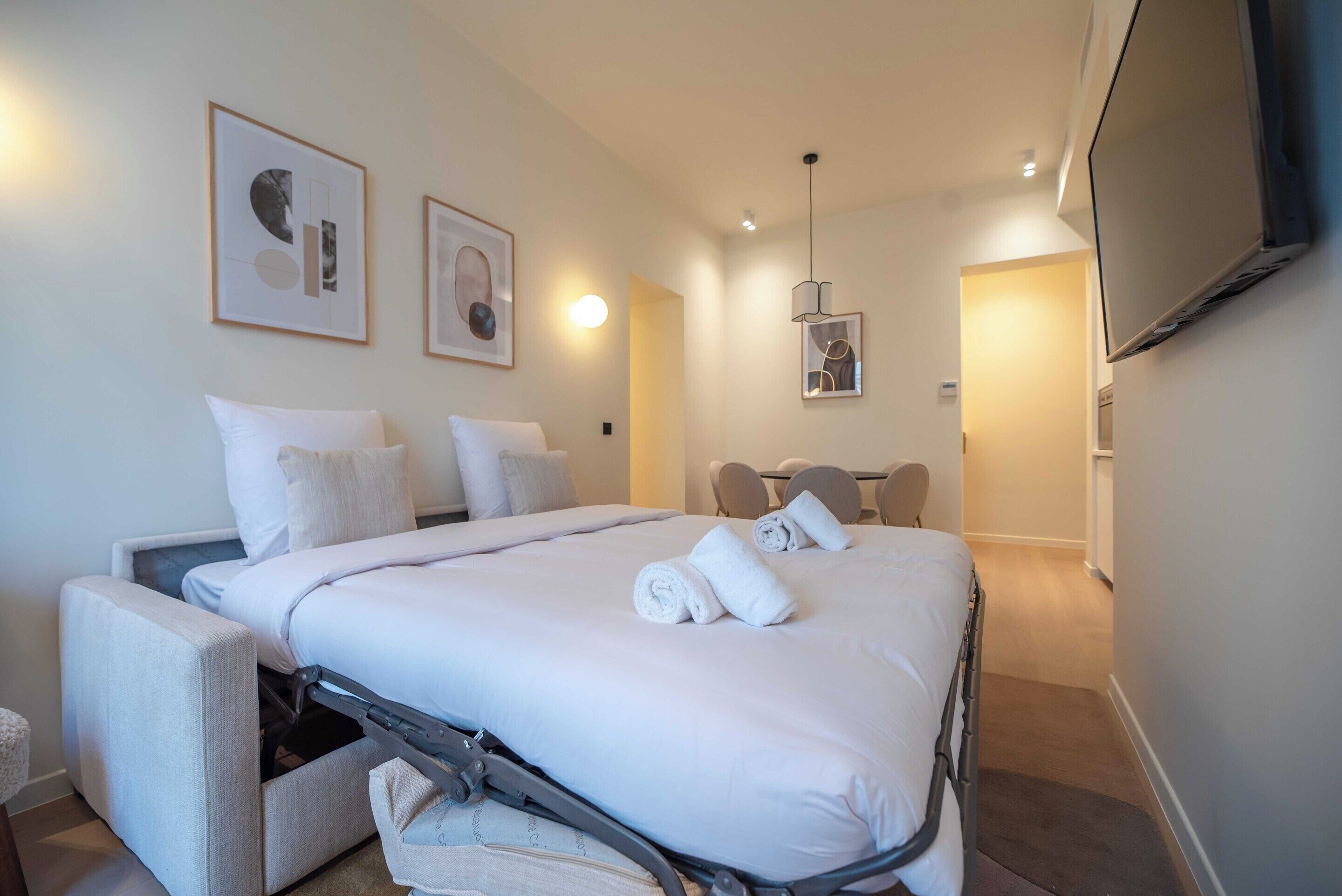 Ein modernes Hotelzimmer mit einem Bett, einem Sessel, einem Fernseher und Kunstwerken an den Wänden.