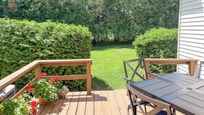 A wooden deck with a table and chairs, surrounded by well-maintained hedges and a lawn.
