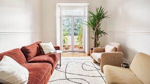 Un salon avec un canapé rouge, un fauteuil beige et une grande plante en pot.