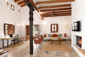 Un ampio soggiorno con pavimento in pietra, travi in legno, camino, televisione e zona pranzo con tavolo e sedie.