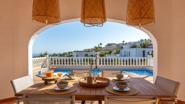 A dining table with a view of a pool and buildings in the background. - Villa CELENZA by Abahana Villas (Benitachell)